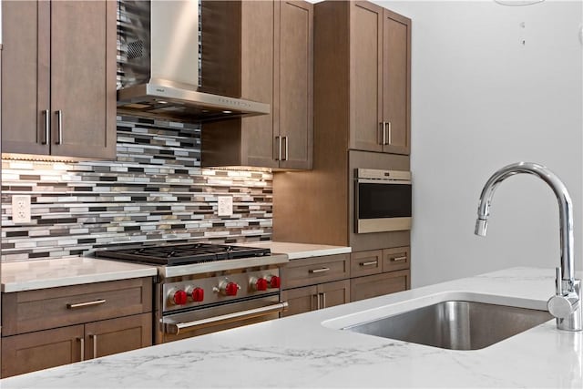 kitchen with wall chimney range hood, a sink, stainless steel stove, tasteful backsplash, and light stone countertops