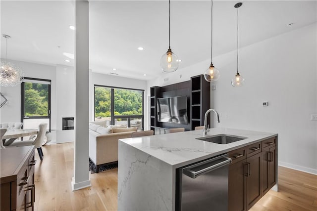 kitchen featuring a sink, stainless steel dishwasher, open floor plan, light wood-style flooring, and light stone countertops