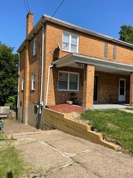 back of property with covered porch, brick siding, and a chimney