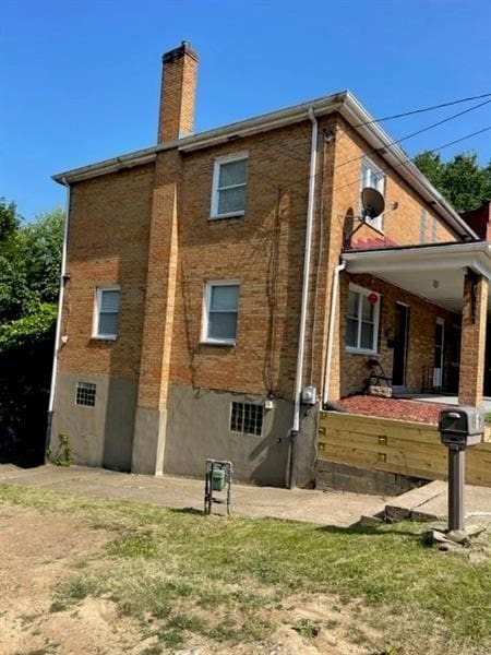 view of side of property featuring brick siding, a yard, and a chimney