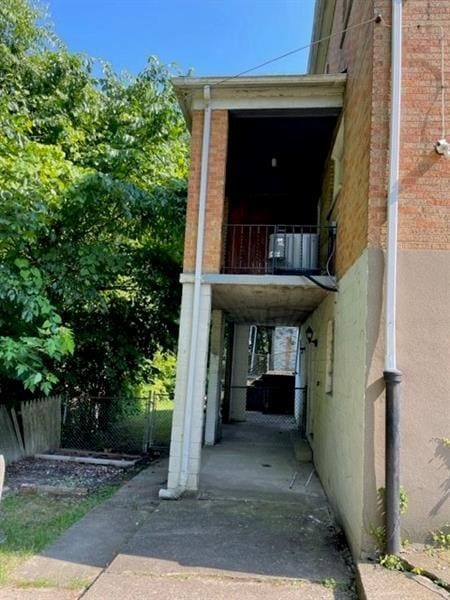 view of exterior entry featuring brick siding, fence, a balcony, and stucco siding