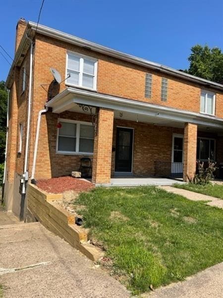 view of front of house with a front yard, covered porch, brick siding, and a chimney