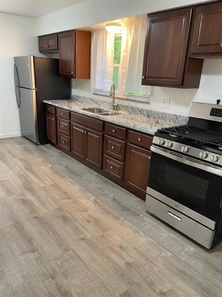 kitchen with appliances with stainless steel finishes, light wood-type flooring, sink, dark brown cabinetry, and light stone counters