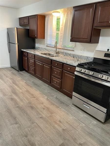 kitchen with stainless steel appliances, light wood-type flooring, a sink, and light stone counters