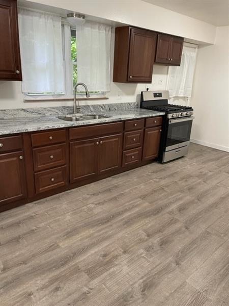 kitchen with stainless steel range with gas cooktop, sink, light wood-type flooring, and light stone counters