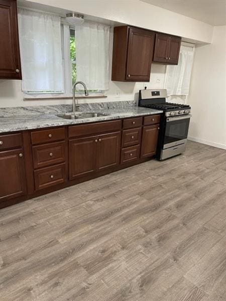 kitchen with light wood finished floors, stainless steel gas range, a sink, and light stone countertops