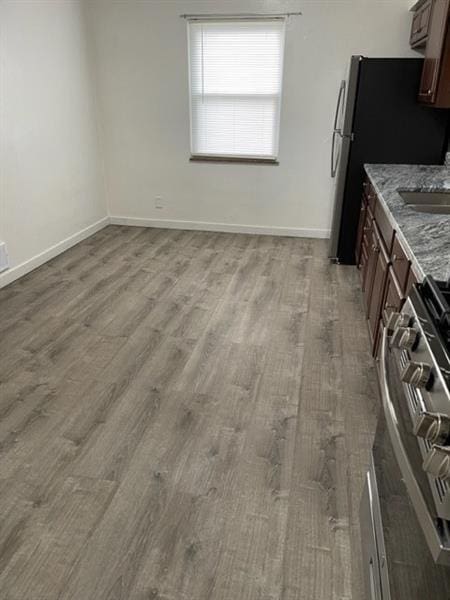 kitchen with stone countertops, stainless steel appliances, a sink, wood finished floors, and baseboards