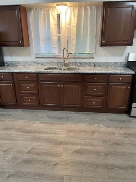 kitchen with sink, stove, light hardwood / wood-style flooring, and light stone counters