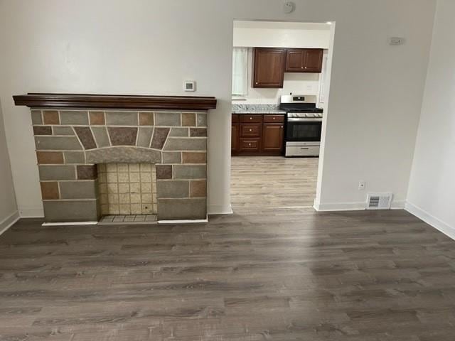 interior space with a fireplace, visible vents, light countertops, dark wood finished floors, and stainless steel range with gas stovetop