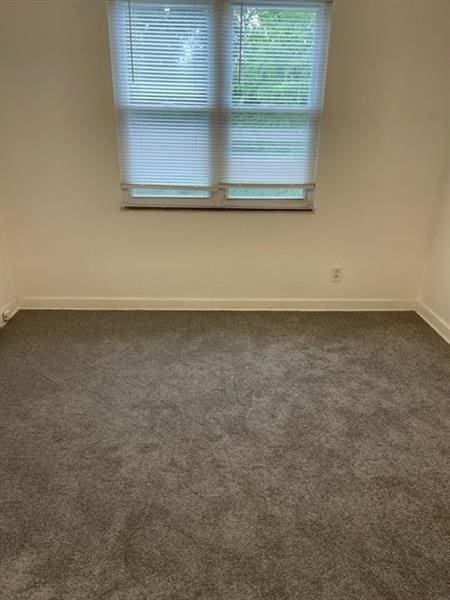 unfurnished room featuring dark colored carpet and baseboards