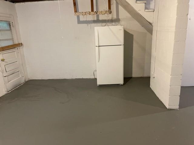 unfinished basement featuring freestanding refrigerator and concrete block wall