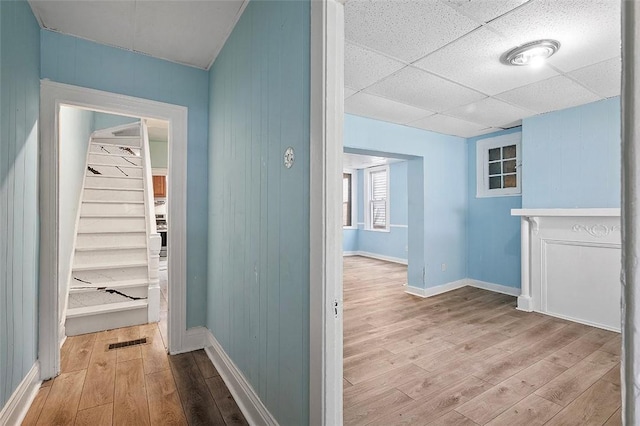 hall with light hardwood / wood-style floors, a drop ceiling, and wood walls