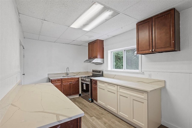 kitchen with a drop ceiling, sink, light hardwood / wood-style flooring, light stone countertops, and stainless steel range