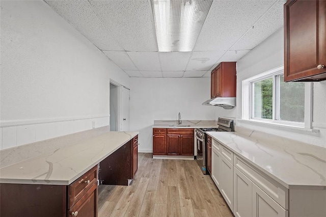 kitchen with light stone countertops, sink, stainless steel range, light hardwood / wood-style flooring, and a paneled ceiling