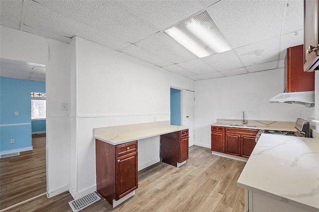 kitchen featuring a paneled ceiling, sink, stainless steel stove, light hardwood / wood-style flooring, and light stone counters