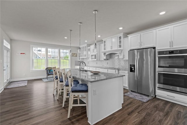 kitchen with light stone counters, stainless steel appliances, an island with sink, and white cabinets