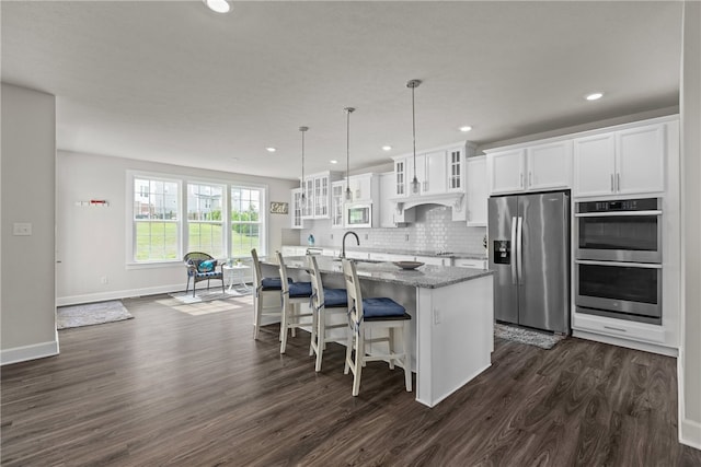 kitchen with dark wood-type flooring, appliances with stainless steel finishes, light stone countertops, a center island with sink, and white cabinetry