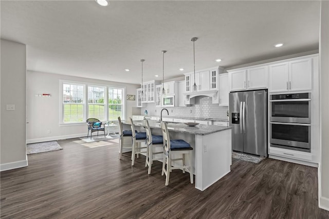 kitchen featuring appliances with stainless steel finishes, a kitchen island with sink, dark hardwood / wood-style floors, light stone counters, and white cabinets