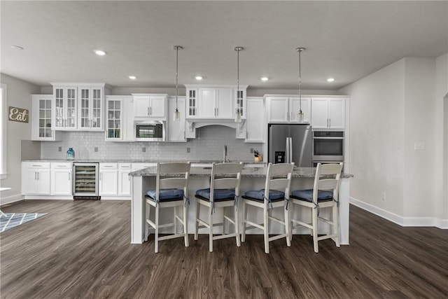 kitchen featuring white cabinetry, a center island with sink, appliances with stainless steel finishes, pendant lighting, and beverage cooler