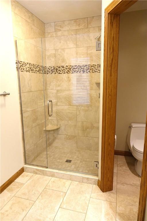 bathroom featuring a shower with door, tile patterned floors, and toilet