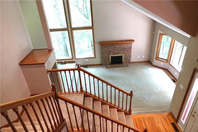 staircase with light hardwood / wood-style flooring, a high ceiling, and a brick fireplace