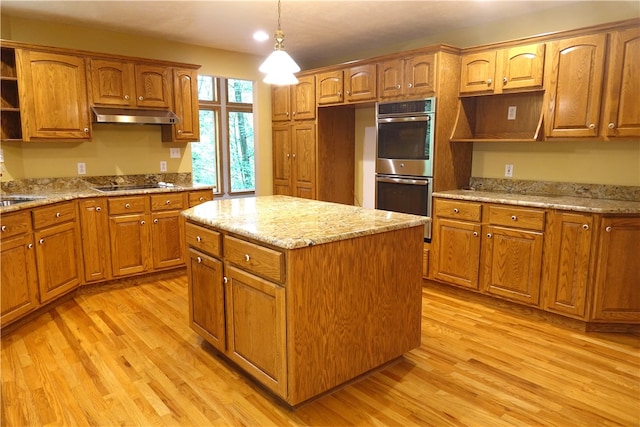 kitchen with stainless steel double oven, hanging light fixtures, light hardwood / wood-style floors, light stone countertops, and a kitchen island