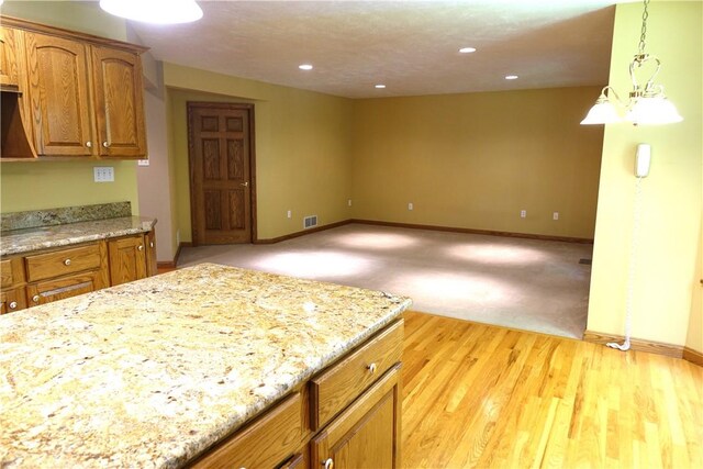 kitchen featuring light stone countertops, light colored carpet, and pendant lighting