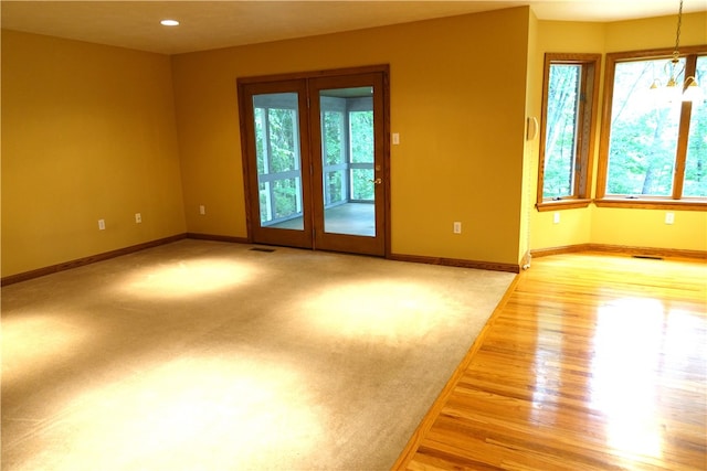 spare room with french doors, a chandelier, light colored carpet, and a wealth of natural light