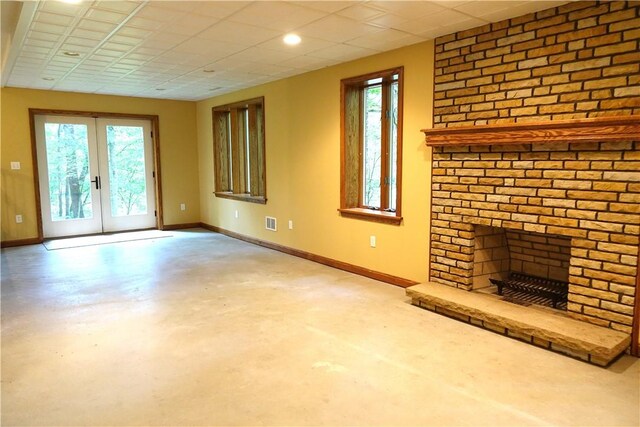 unfurnished living room featuring concrete floors, a brick fireplace, french doors, and a wealth of natural light