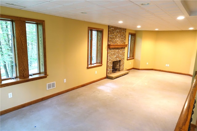 unfurnished living room featuring a drop ceiling, a healthy amount of sunlight, a brick fireplace, and brick wall