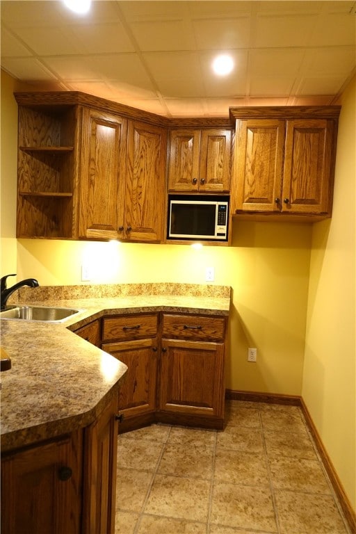 kitchen featuring a paneled ceiling, stainless steel microwave, sink, and light tile patterned flooring