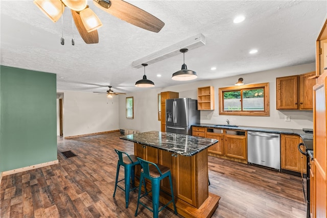 kitchen with a kitchen bar, dark hardwood / wood-style floors, ceiling fan, appliances with stainless steel finishes, and a kitchen island