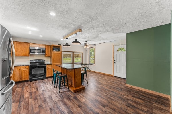 kitchen with dark hardwood / wood-style floors, ceiling fan, a breakfast bar area, and stainless steel appliances