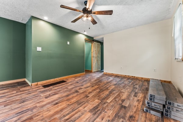 unfurnished room with a textured ceiling, a barn door, hardwood / wood-style floors, and ceiling fan