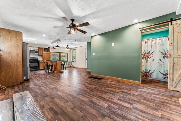 living room with ceiling fan, a barn door, dark wood-type flooring, and a textured ceiling