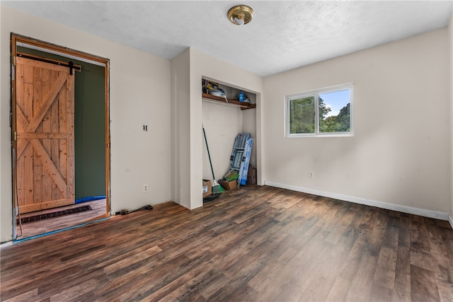 unfurnished bedroom with a textured ceiling, dark hardwood / wood-style floors, a barn door, and a closet