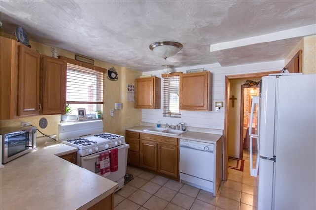 kitchen with a sink, white appliances, light tile patterned floors, and light countertops