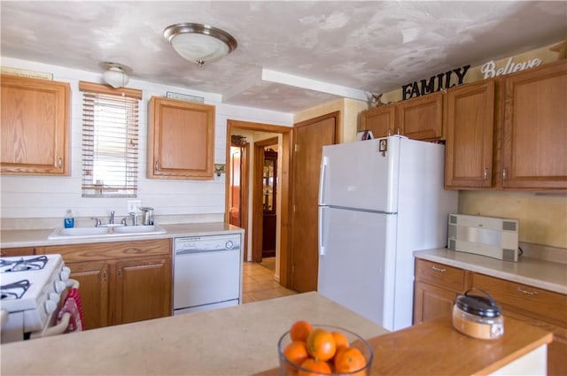 kitchen with brown cabinetry, white appliances, light countertops, and a sink