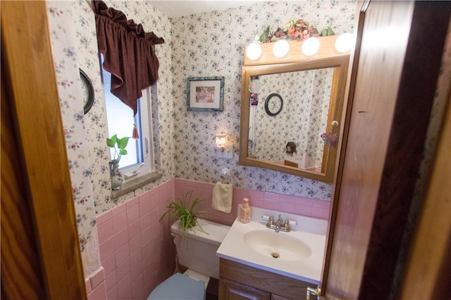 bathroom with a wainscoted wall, toilet, tile walls, wallpapered walls, and vanity