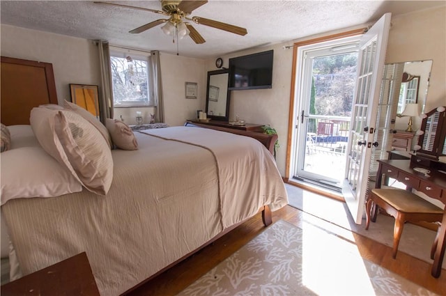 bedroom with access to exterior, multiple windows, a textured ceiling, and wood finished floors