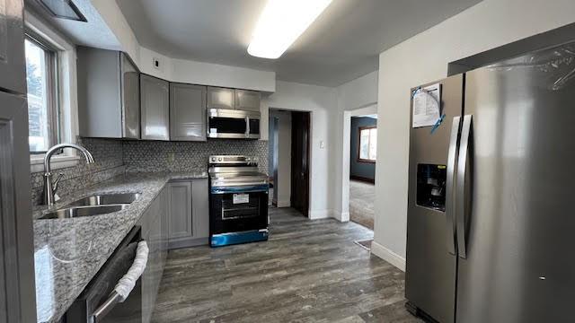 kitchen with stone counters, gray cabinets, decorative backsplash, sink, and appliances with stainless steel finishes