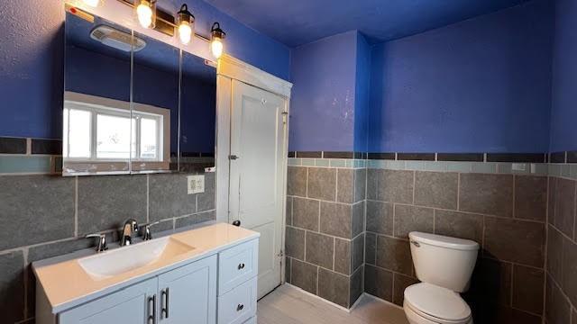 bathroom with toilet, vanity, and tile walls