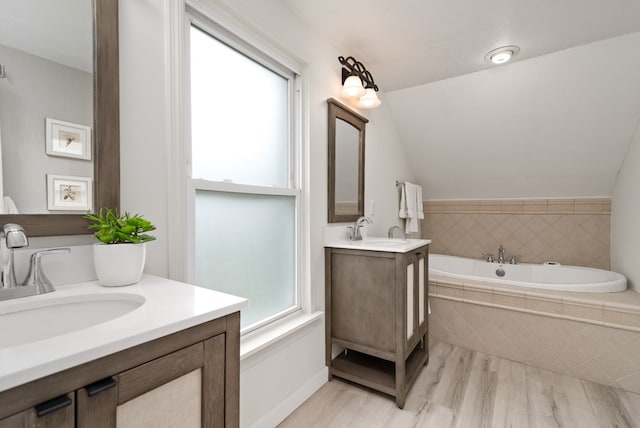 bathroom with double vanity, tiled tub, wood-type flooring, and a wealth of natural light