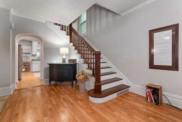 stairway with ornamental molding and light hardwood / wood-style floors