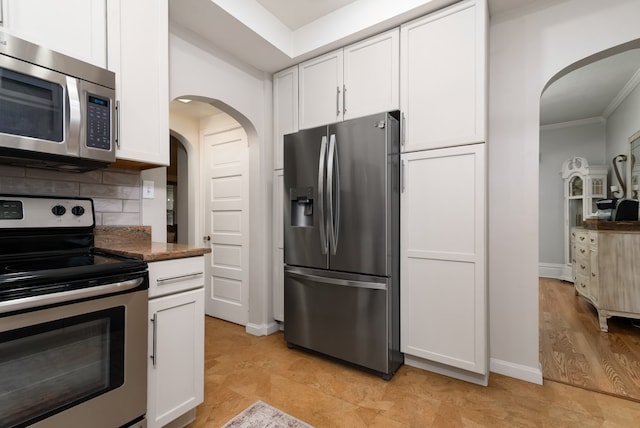 kitchen with appliances with stainless steel finishes, dark stone countertops, white cabinetry, backsplash, and light hardwood / wood-style flooring