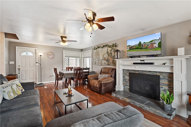 living room featuring ceiling fan, dark hardwood / wood-style flooring, and a stone fireplace