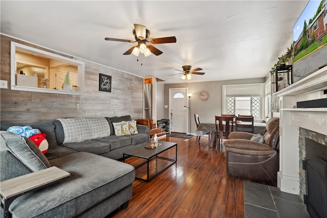 living room with ceiling fan, a tiled fireplace, tile walls, and dark hardwood / wood-style flooring