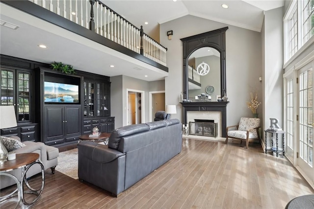 living room featuring high vaulted ceiling, visible vents, a fireplace with raised hearth, and wood finished floors