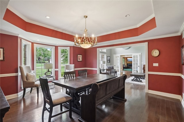 dining space with crown molding, dark hardwood / wood-style flooring, a tray ceiling, and a chandelier