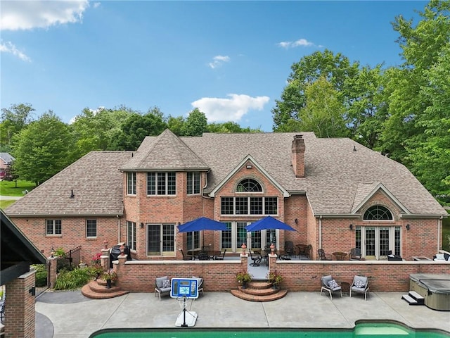 rear view of house with a hot tub, a chimney, roof with shingles, a patio area, and brick siding